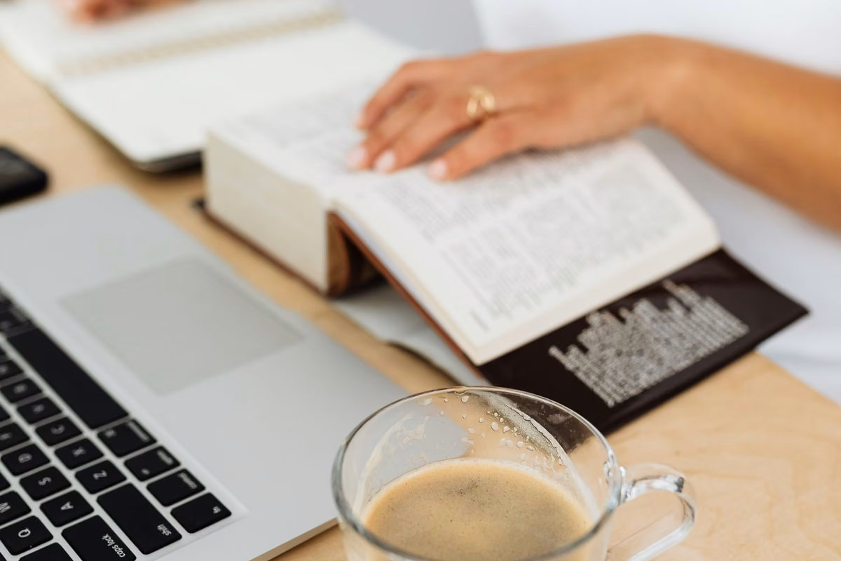 Personne écrivant calmement dans un carnet à côté d’un ordinateur portable et d’un café